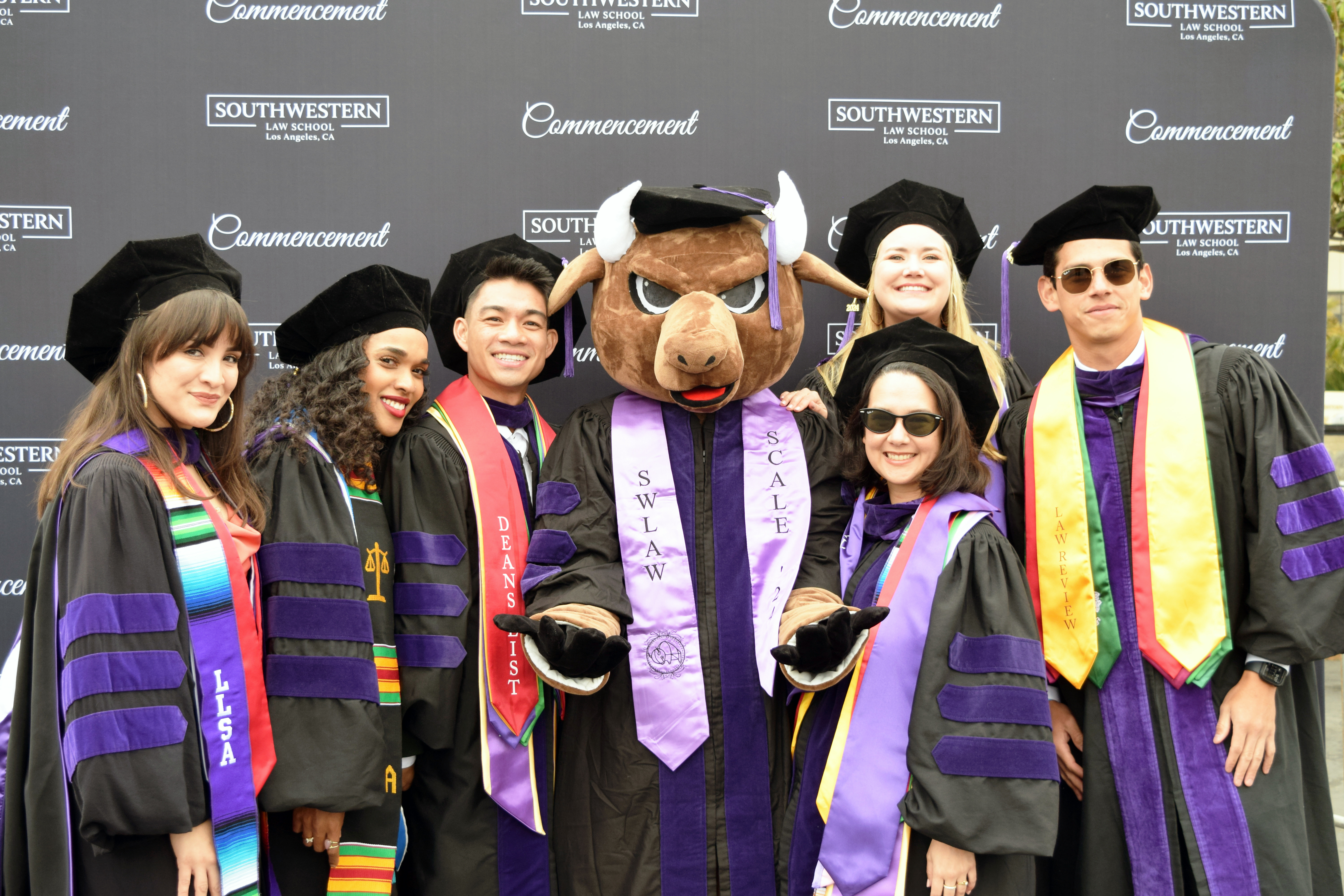 Group of students in commencement regalia posing with Bison mascot