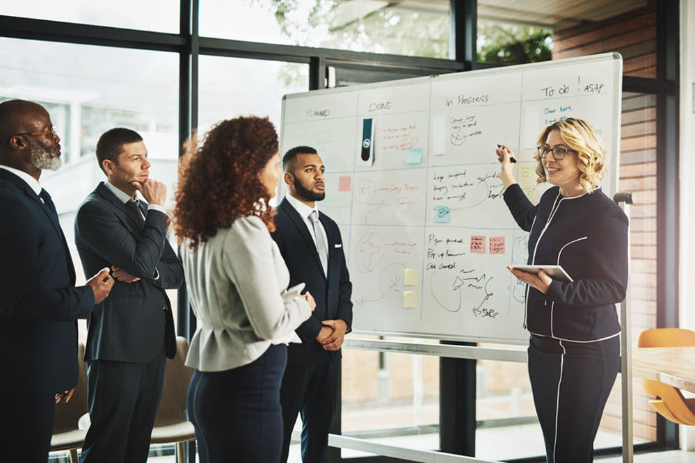 Woman at whiteboard speaking to peers