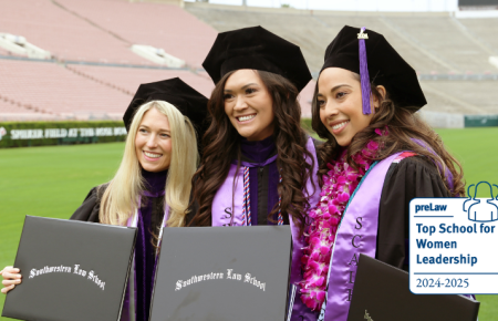 Three female students in commencement robes smiling with their diplomas with the Top School for Women Leadership preLaw badge on bottom right hand corner